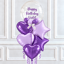 Purple and lavender birthday balloon bouquet with a clear round balloon reading 'Happy Birthday Violet,' including heart, star, and round foil balloons, set against a white paneled wall.